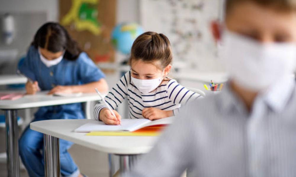 Masked students writing while in the classroom 