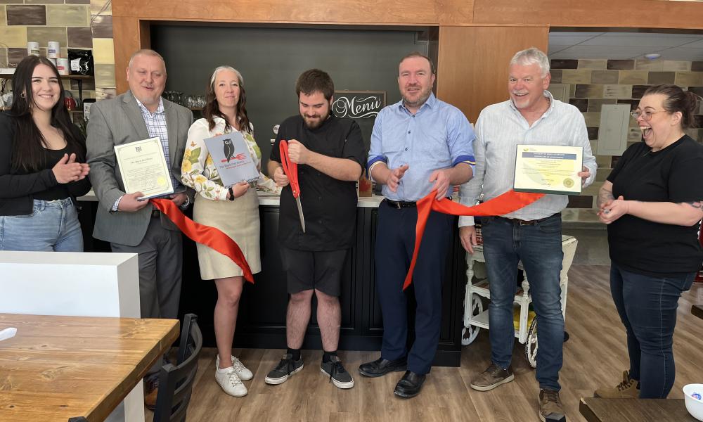 An image showing a group of people cutting a red ribbon to mark the opening of The Black Owl Bistro