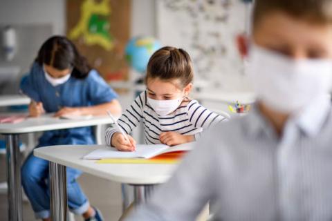 Masked students writing while in the classroom 