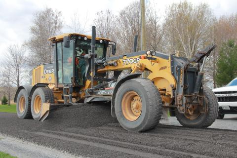 A municipal grader is seen leveling gravel on a road