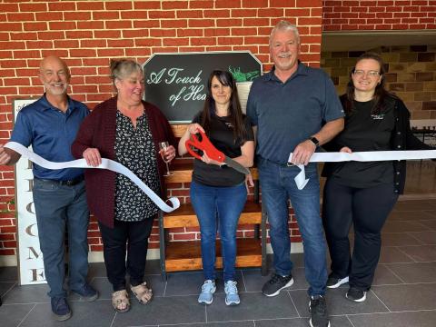 A group of people cut a ribbon for the grand re-opening of A Touch of Health